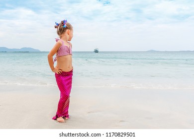 Little beautiful girl dressed in swimsuit as a mermaid stands on the seashore.