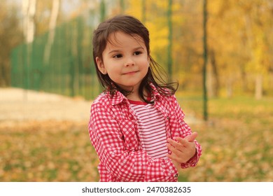 A little beautiful girl in a flat T-shirt and a plaid shirt enjoys playing in the autumn park. The concept of children's happiness in nature. Bright explosion of colors - Powered by Shutterstock