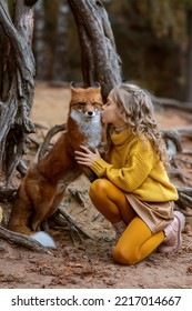 Little beautiful girl with a fox in the autumn forest. Friendship of a girl and a fox. Love of wild animals. Caring for wild animals.