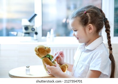 A little beautiful girl makes a vaccination to a teddy bear in her hand, the concept of vaccinating children against coronavirus, health care, the girl plays a role-playing game