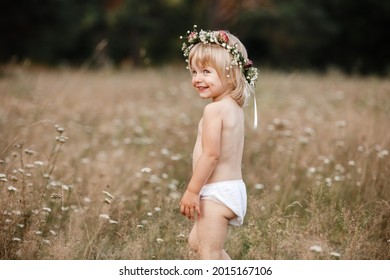 Little Beautiful Girl On Nature On Summer Day Vacation. Childgirl In Panties And A Flowers Wreath On Her Head Is Playing In The Field On Summer Day. The Concept Of Family Holiday And Time Together.