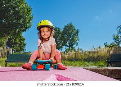 Little Beautiful Girl Sit On The Skate Playing At Skatepark Wearing Helmet On Sunny Summer Day