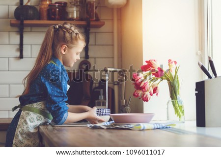 little beautiful girl washes dishes at home in the kitchen