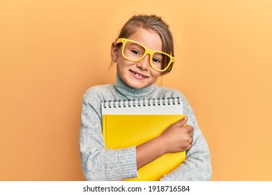 Little beautiful girl wearing glasses and holding books smiling with a happy and cool smile on face. showing teeth. 