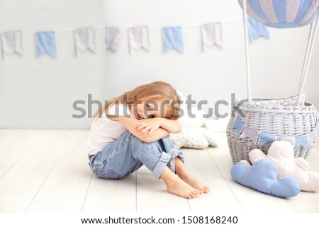 Little beautiful girl in a white T-shirt and jeans sits on the background of a decorative balloon. The child plays in the children's room. The concept of childhood, travel. birthday holiday decoration