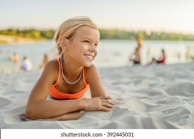 Little beautiful smiling girl lying on the sand at the beach.