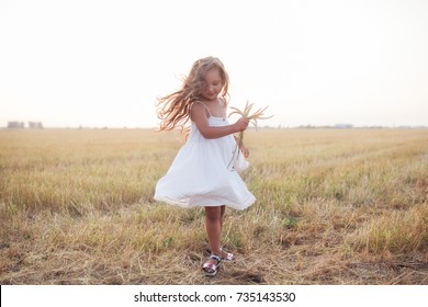 Little beautiful smiling girl on a gold wheat field walking at sunset. Happy five years old girl smiling and laughing in summer day at nature. Happiness freedom and carefree childhood concept