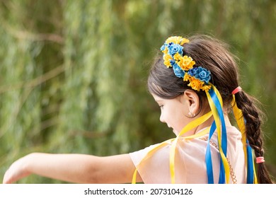 Little beautiful smiling girl in Ukrainian national wreath decoration stands on the shore of the pond