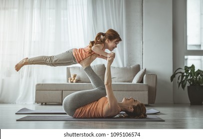 Little bird. Mother is lying on her back and holding her daughter on her feet during fitness at home. Girl looking happy while woman is laughing 