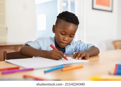 Little black boy sitting on table and painting with colored marker on book. Cute african american child drawing in the living room at home. Schoolboy colouring in book with red marker at home. - Shutterstock ID 2114224340