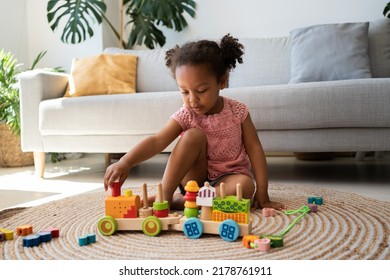 Little black girl engaged in game, playing with wooden building railway station, resting on heating floor at home, enjoying comfort, leisure. African american child playtime and activity concept - Shutterstock ID 2178761911