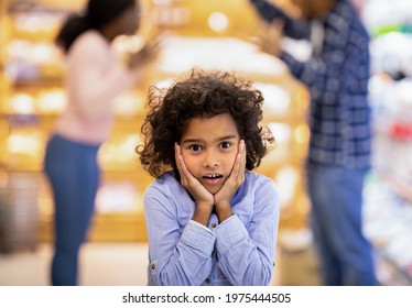 Little Black Girl Feeling Shocked While Her Parents Arguing At Big Shopping Mall. Emotional African American Kid Cannot Tolerate Her Mom And Dad's Conflict At Grocery Store