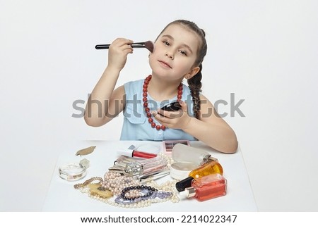 little black-haired girl is playing with makeup. funny photo shoot in the studio on a white background.
