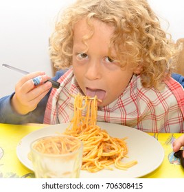 A Little Blond Boy Eating Pasta With Tomato Sauce