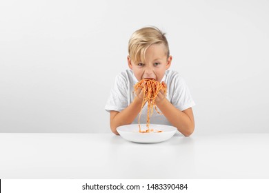 little blond boy in front of white background eats spaghetti and