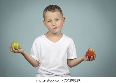 little, blond boy holding an apple and a pear in his hand, in front of a green background