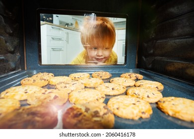 Little blond boy look through the oven door glass with cookies being baked inside - Powered by Shutterstock