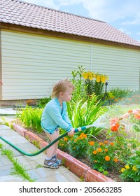 little blond boy pours water from a hose in the garden plant