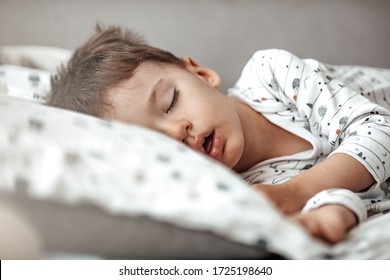 Little Blond Boy Sleeping In His Bed. Restless Sleep Of A Baby With A Cold. The Kid Sleeps With His Mouth Open. My Little Boy Sleeping By The Light Of The Window.