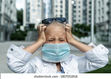 Little Blond Caucasian Girl Wearing Protective Face Mask Feel Stressed And Unhappy Screaming And Crying Due Quarantine And Covid-19 Pandemic New Normal. Upset Exhausted Child Walk City Street Outdoor