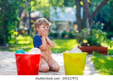 Little blond child boy having fun with splashing water in summer garden. Kid making water bombs and playing with family. Outdoor leisure with kids on hot summer day.