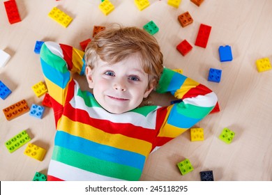 Little blond child playing with lots of colorful plastic blocks indoor. Kid boy wearing colorful shirt and having fun with building and creating.