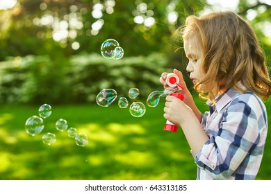 A little blond girl blows soap bubbles in a park