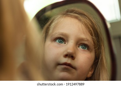 Little Blond Girl With Blue Eyes Looking In The Mirror. Cute Serious Curious Child Admires Herself In Reflection. Kids Home Portrait In Daylight Near Window. Growing Up Psychology Personal Development