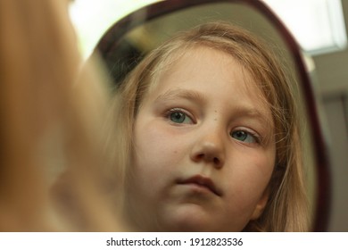 Little Blond Girl With Blue Eyes Looking In The Mirror. Cute Serious Curious Child Admires Herself In Reflection. Kids Home Portrait In Daylight Near Window. Growing Up Psychology Personal Development