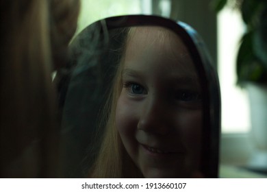 Little Blond Girl With Blue Eyes Looking In The Mirror. Cute Serious Curious Child Admires Herself In Reflection. Kids Home Portrait In Daylight Near Window. Growing Up Psychology Personal Development