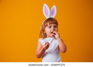 Little Blond Girl With Dirty Chocolate Bunny Ears Eating Easter Egg