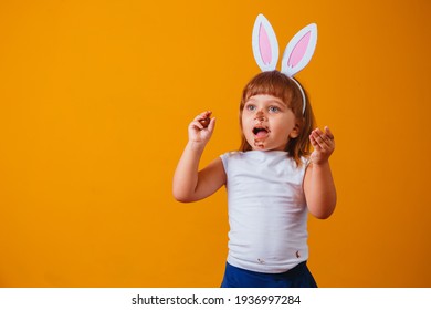 Little Blond Girl With Dirty Chocolate Bunny Ears Eating Easter Egg