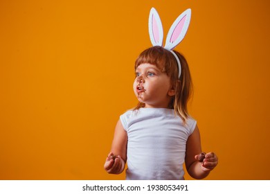 Little Blond Girl With Dirty Chocolate Bunny Ears Eating Easter Egg