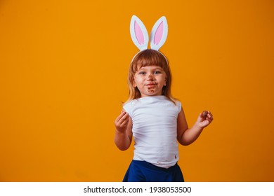 Little Blond Girl With Dirty Chocolate Bunny Ears Eating Easter Egg