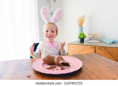 Little Blond Girl With Dirty Chocolate Bunny Ears Eating Easter Egg