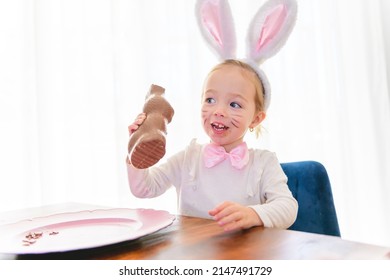 Little Blond Girl With Dirty Chocolate Bunny Ears Eating Easter Egg