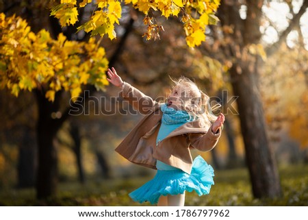 Little blond girl jumping to the autumn leaves in the park. Cute girl have fun on a warm sunny day. Happy emotions, outdoor activities in autumn. Selective focus.