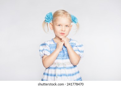 Little Blond Girl On A White Background Standing With Folded Hands