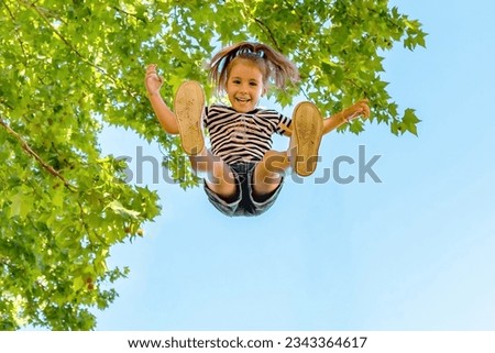 Little blond girl in striped t-shirt jumping in the air. Childish games. Girl in the air smiling and looking at camera.