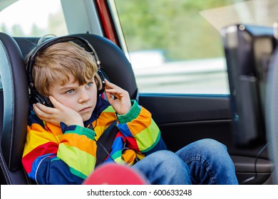 Little Blond Kid Boy Watching Tv Or Dvd With Headphones During Long Car Driving On Family Vacations. Leisure For Children For Long Drive. Preschool Child Sitting In Safe Car Seat.