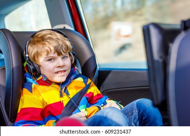 Little Blond Kid Boy Watching Tv Or Dvd With Headphones During Long Car Driving On Family Vacations. Leisure For Children For Long Drive. Preschool Child Sitting In Safe Car Seat.