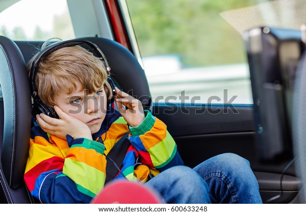 Little blond\
kid boy watching tv or dvd with headphones during long car driving\
on family vacations. Leisure for children for long drive. Preschool\
child sitting in safe car\
seat.