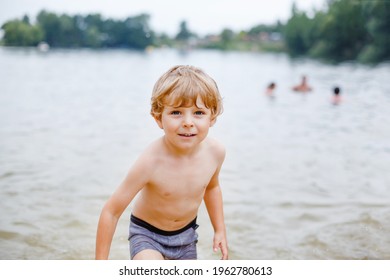 Little Blond Preschool Boy Having Fun With Splashing In A Lake On Summer Day, Outdoors. Happy Child Learning Swimming. Active Leisure With Kids On Vacations. Danger On Domestic Lakes