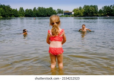 Little blond preschool girl having fun with splashing in a lake on summer day, outdoors. Happy child learning swimming. Active leisure with kids on vacations. Danger on domestic lakes.