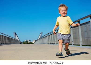 Kleiner blonder Kleinkind-Junge läuft auf der Fußgängerbrücke und lächelt
