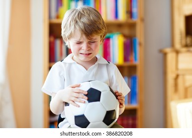 Little Blond Toddler Kid Boy With Ball Watching Soccer European Cup Game On Tv. Sad Crying Child About Lost Game Of His Football Team. Champions League Concept.