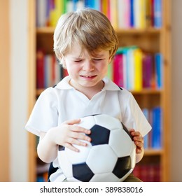 Little Blond Toddler Kid Boy With Ball Watching Soccer European Cup Game On Tv. Sad Crying Child About Lost Game Of His Football Team. Champions League Concept.