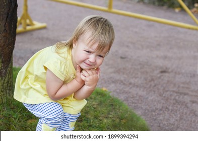 Little Blonde Baby Girl In A Yellow Dress Crying In The Park. Child Stomach Ache Pain. Sad, Depressed And Upset Girl Cries Outdoor. Tantrums And Whims Of Children. Child Emotions And Capricious