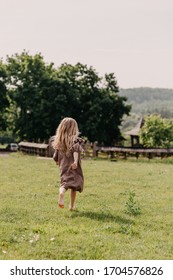 Little blonde barefoot girl, running on grass in the backyard, field, wearing a brown vintage dress.