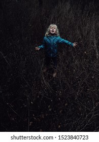 Little Blonde Caucasian Scared Girl Lost In Wood Forest Looking Up Above. Child Cry Scream Ask For Help. Concept Of Lost  Abandoned Kid Left Alone In Trouble Problem. 